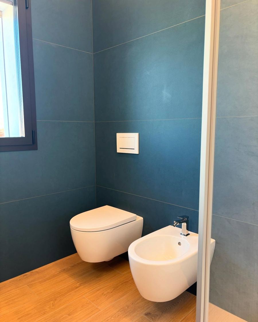 Baño azul con sanitarios suspendidos y suelo de madera
