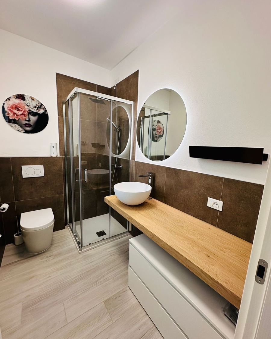 Baño con mampara, espejo redondo y encimera de madera